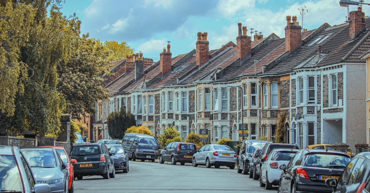 Picturesque view of parked cars along classic English townhouses under a blue sky.